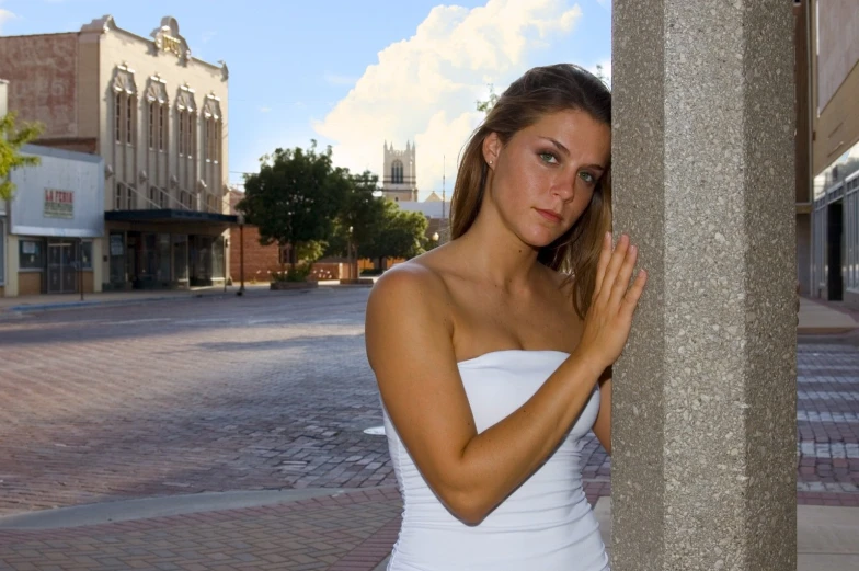 a  in a white dress leaning against a pillar