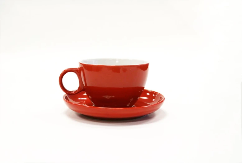 a red coffee cup and saucer sitting side by side