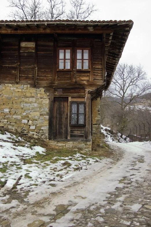 a dirt road next to a snow covered hill and old cabin