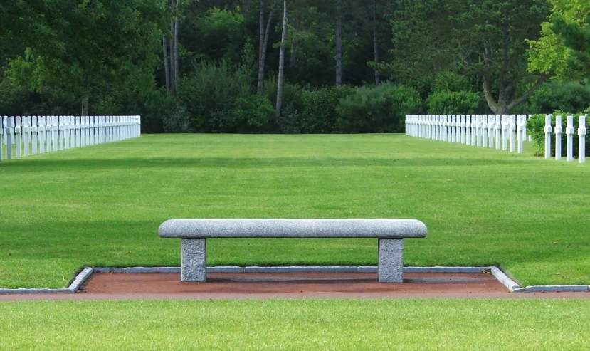 bench sits alone in a grassy area that has white picket fenced in