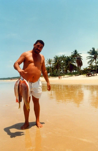 a man on the beach holding a fish