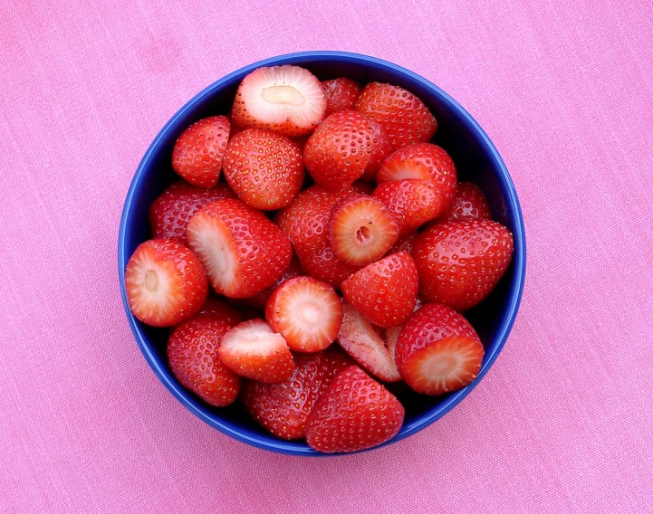 a blue bowl full of strawberries on a pink surface