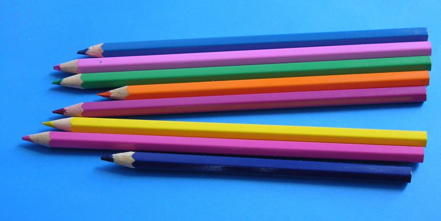 five pencils on a blue surface, in all rainbow colors