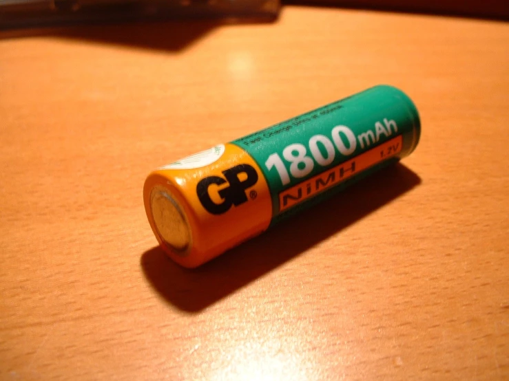 an orange aa battery laying on top of a wooden table