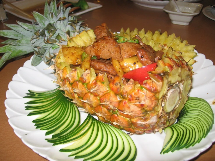 a pineapple with chopped pineapple, sliced kiwi and sliced carrots on a plate