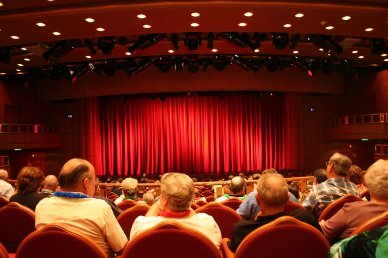 an auditorium with red curtains and seated audience