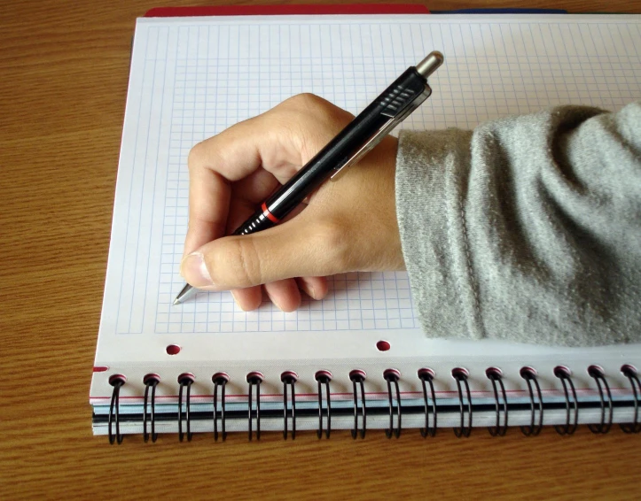 a hand with a pen that is near a notebook