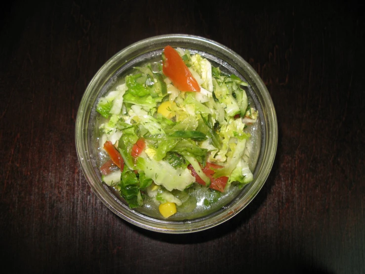 a glass bowl filled with salad on top of a wooden table