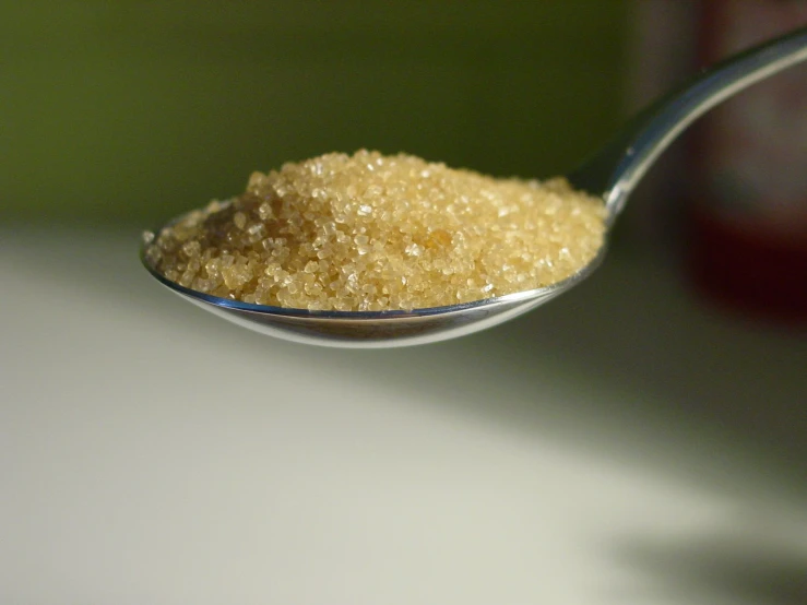 a spoon filled with sugar sits on a white surface