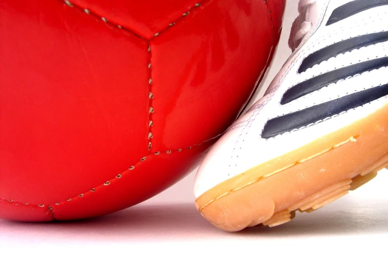 a close up view of a white and black soccer shoe on top of a red soccer ball