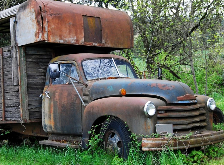 an old truck sitting in the grass near trees
