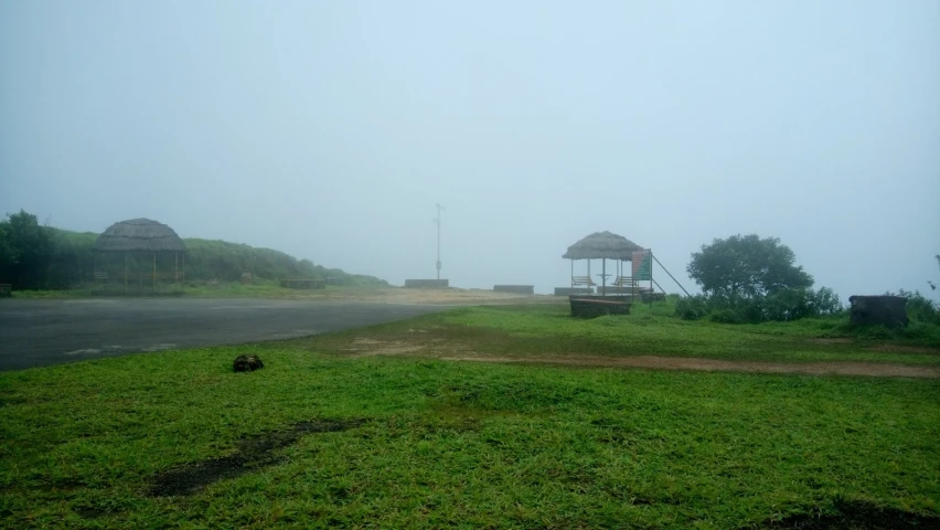 a foggy and grassy area with benches, and huts