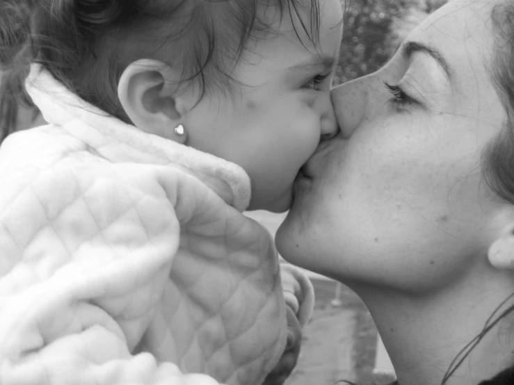 the woman holds the child and kisses it on a cheek