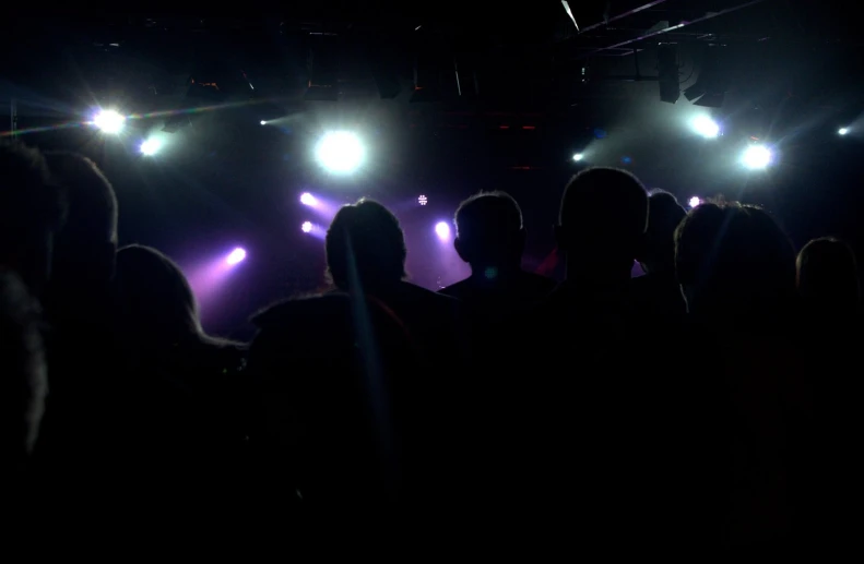 people sitting in front of a dark stage with light coming from the spotlight