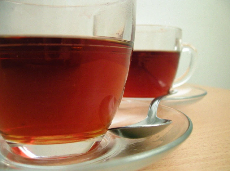 two glasses of tea sit on a saucer with spoons