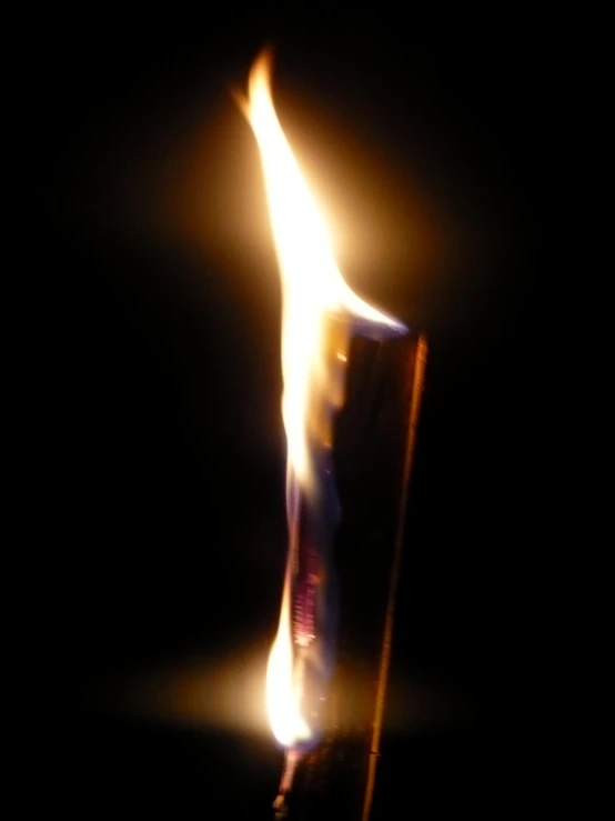a candle lit with bright flames as it is dark