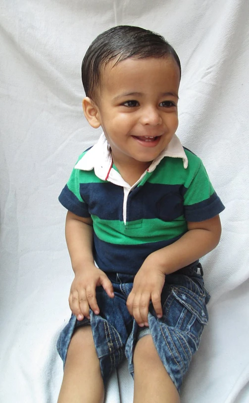 a boy with a green and blue shirt is sitting on a white sheet