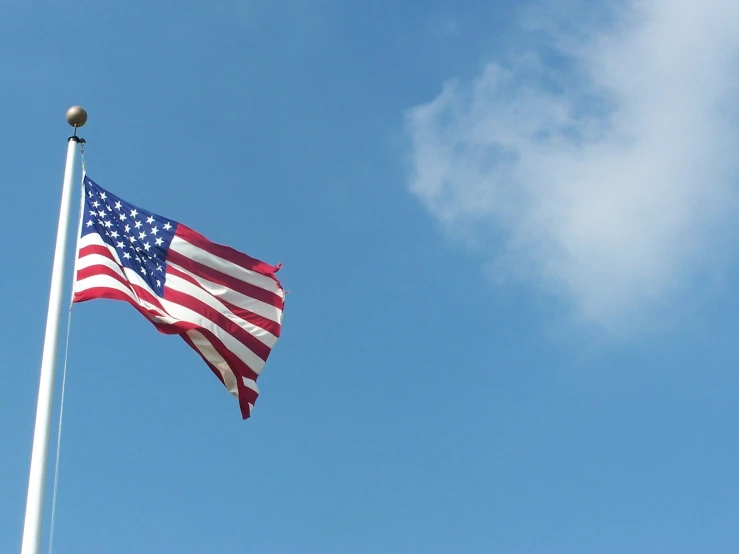 a large american flag on a pole flying in the sky