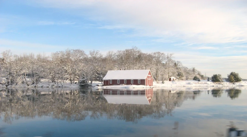 a red barn with a snow covered roof sits on the shore of a frozen lake