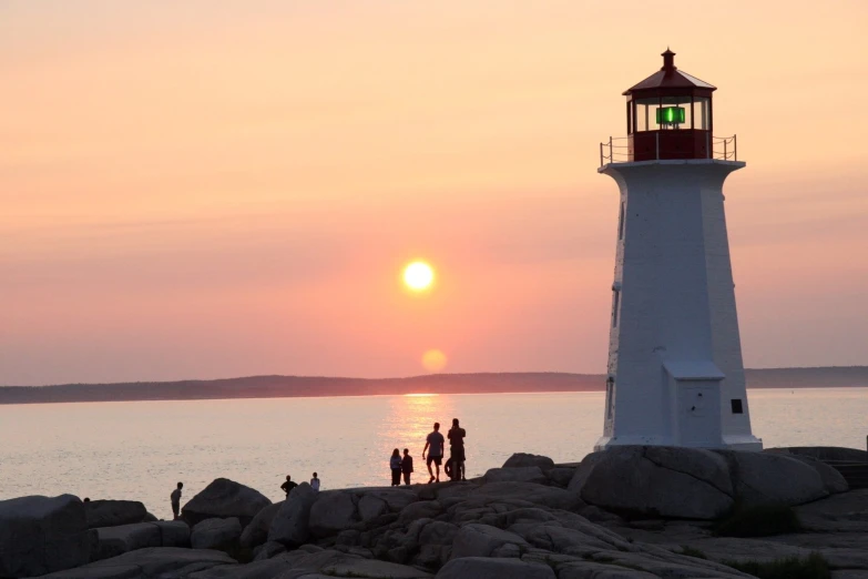 people stand on rocks near the water at sunset