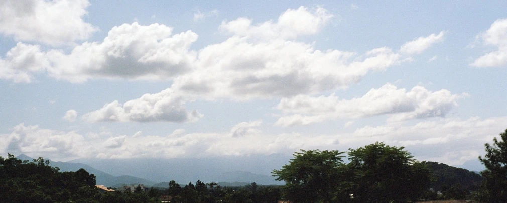 a large white clouds over trees on a hill