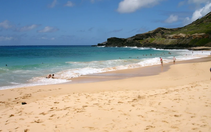 a sandy beach covered in water next to a lush green hillside
