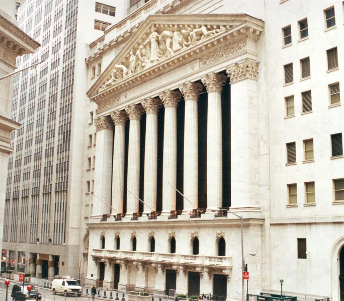 an old, white building with columns on its front and a few people walking across the street