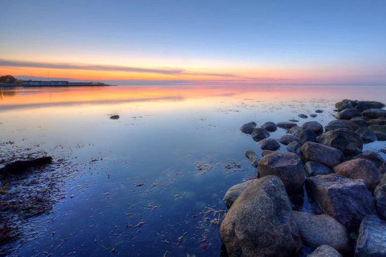 rocky shoreline with water reflecting the sunset and a large building in the distance