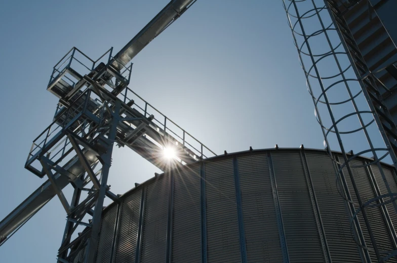 the sun shining through the sky over a large grain tank