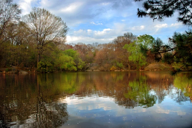 the pond has water reflection, some trees and clouds