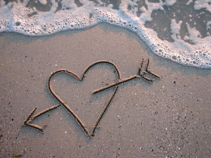 there is a heart on a beach, shaped by an arrow