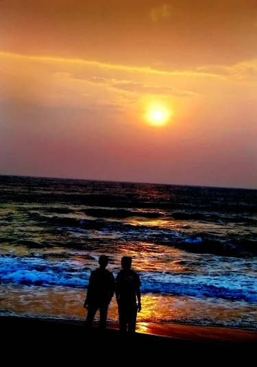 two people walking on the beach while watching the sunset