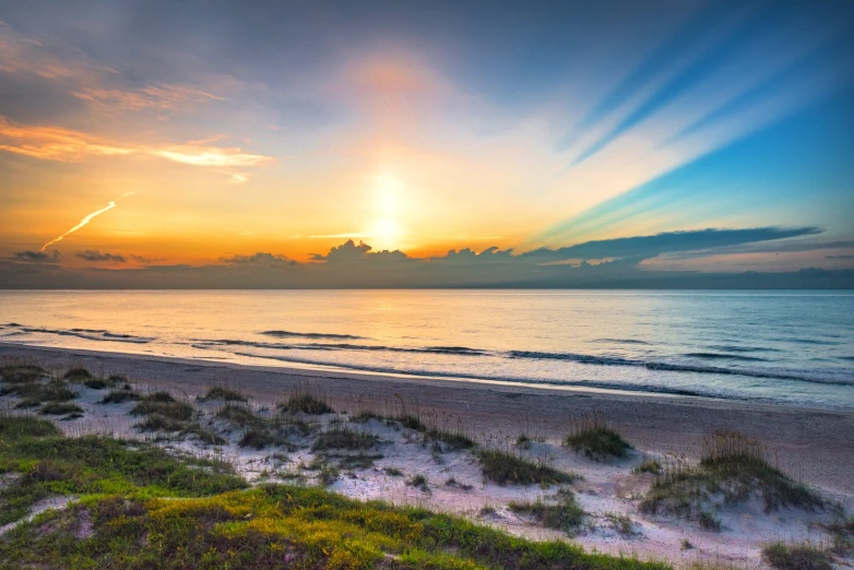 the sun is rising over the ocean off of the beach