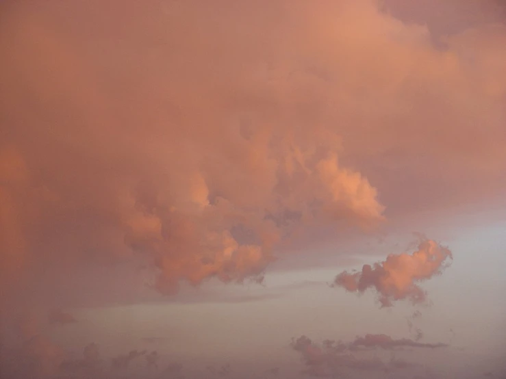 large, pink clouds are above the beach and an airplane