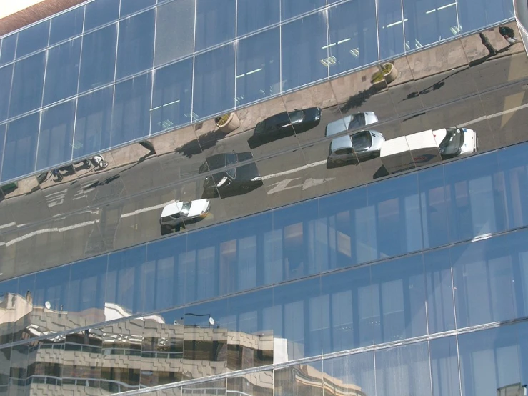 the top of a glass building with cars and buildings in the reflection