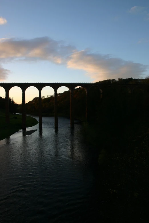 a train bridge sitting above a river next to a lush green hillside