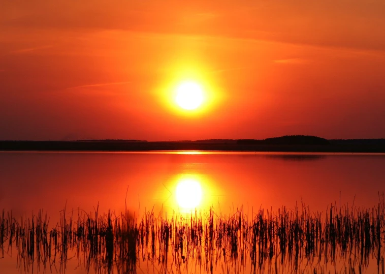 a sun rises over the horizon as it reflects in a lake