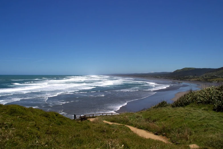 a beach near a hill with waves crashing on the shore