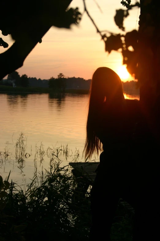 the person sits on the shore as the sun sets