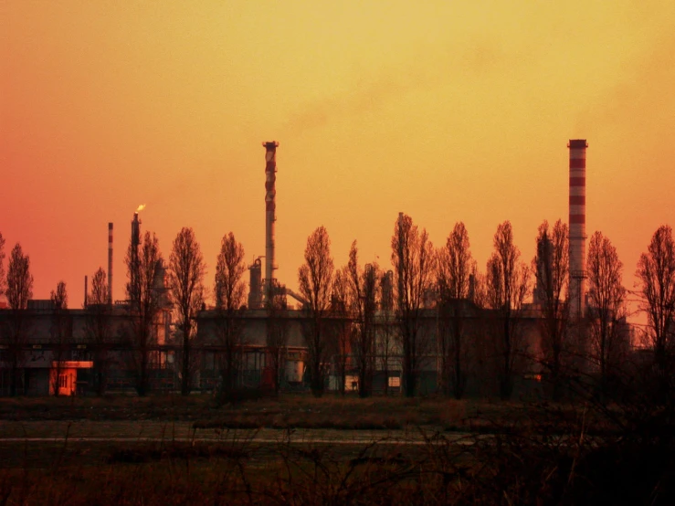 the factory towers are seen in silhouette as the sun sets