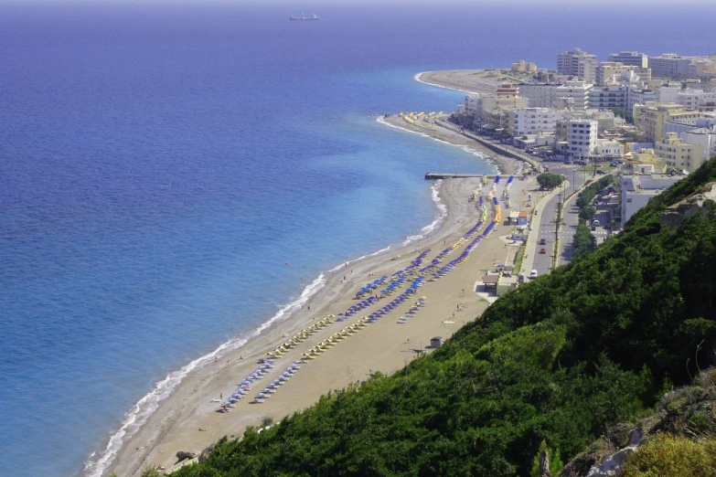 a beach with many umbrellas in the shade and a city in the background