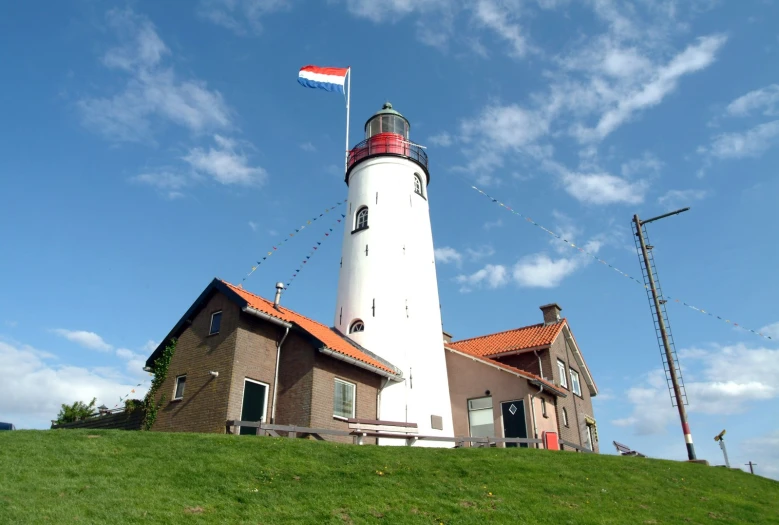 a lighthouse sits near two buildings on a hill