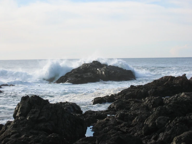 a large wave breaks into the rocky ocean