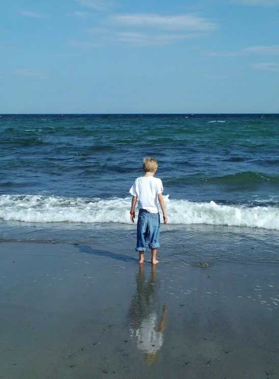 a small boy on the beach looking out to the ocean