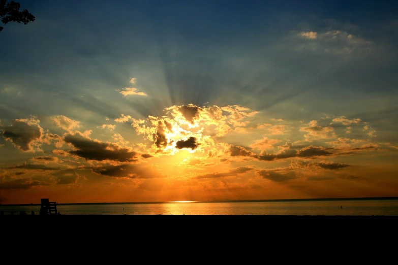 sun coming out over the ocean with a bench in front of it