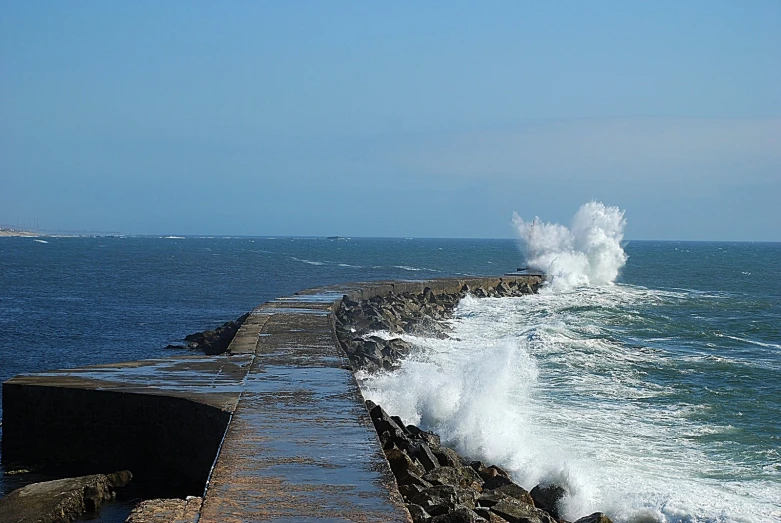 an ocean wave hitting rocks near a pier