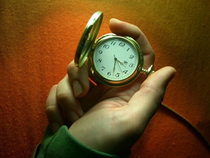 a person holds a gold pocket watch on the end of a key chain