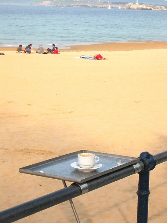 a small cup is placed on a metal bar next to the beach