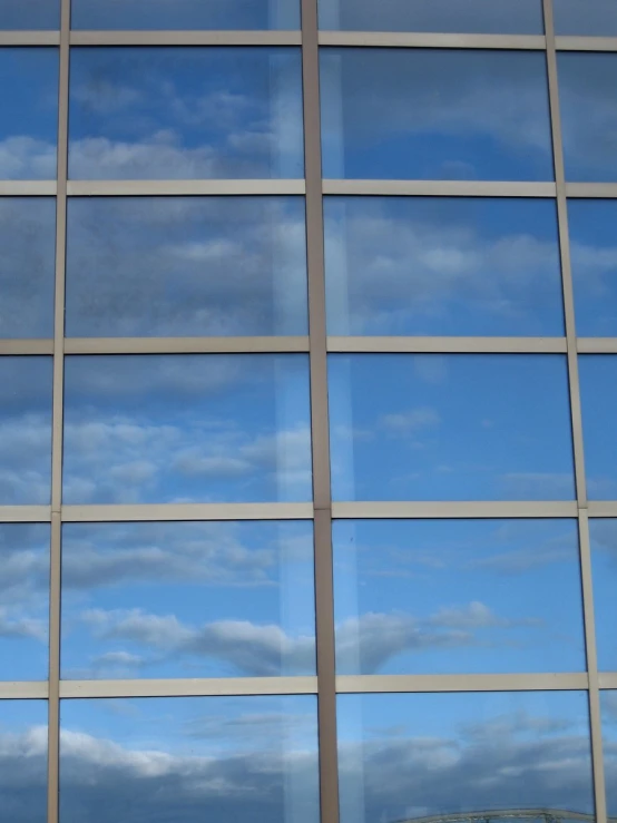 an airplane flying through the clouds reflected in a glass building