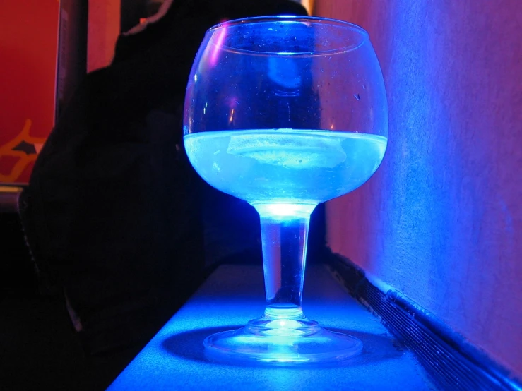 a blue wine glass next to a person in a dark room